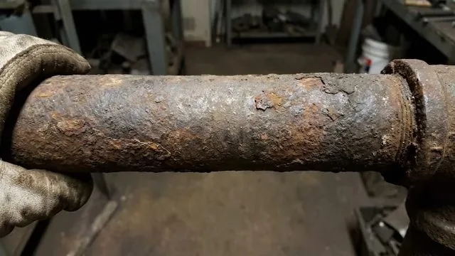 Gloved hands holding a rusty galvanized pipe section