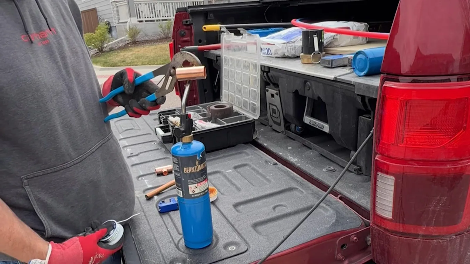 Plumber standing at an open truck bed with a torch, pliers and a tool organizer